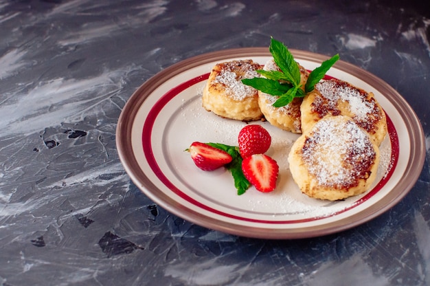 curd pancakes with strawberries mint and icing sugar in a white plate. 