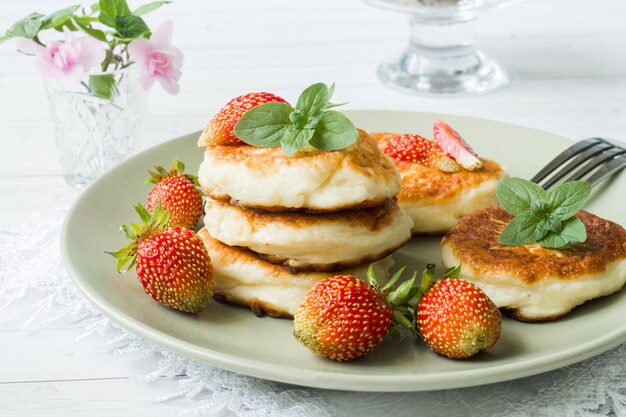 Curd pancakes with strawberries and mint on a plate.