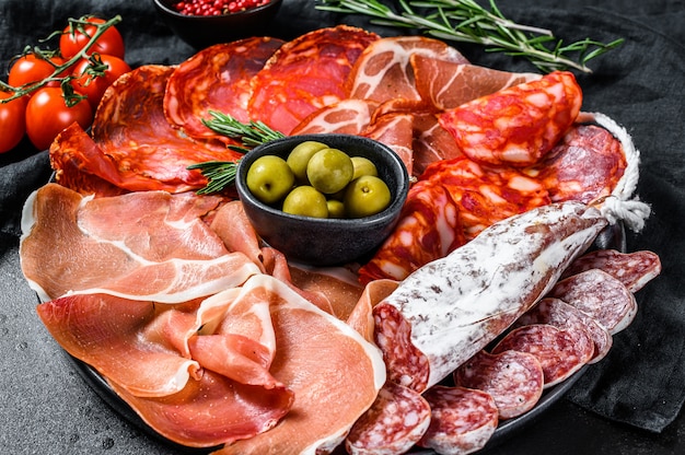 Cured meat platter of traditional Spanish tapas. Chorizo, jamon serrano, lomo and fuet. Black background. Top view.