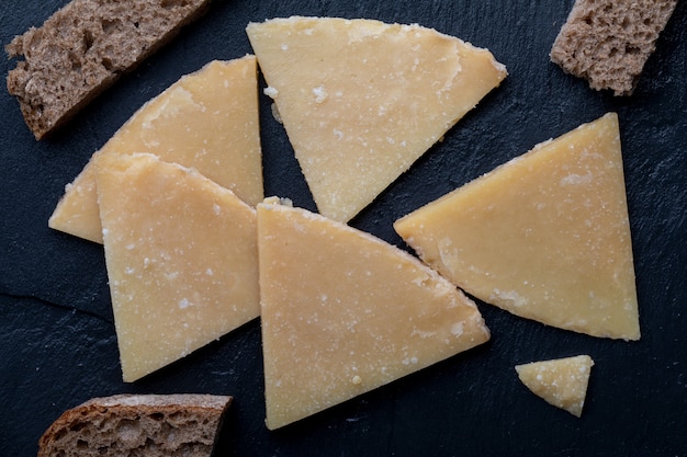 Cured sheep cheese. Cut into pieces on black board and bread. Cheese fork. Top View.