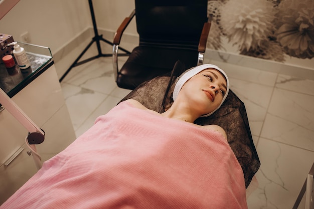 Curing skin problems Cropped female cosmetologist looking at client's face through magnifying lamp examining her skin Happy relaxed young woman getting professional facial treatment in spa salon
