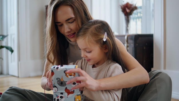 Curious baby opening gift at New Year house Mom presenting toy to daughter