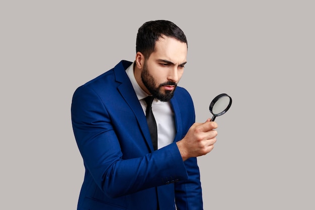 Photo curious bearded man looking through magnifying glass finding out something exploring inspecting