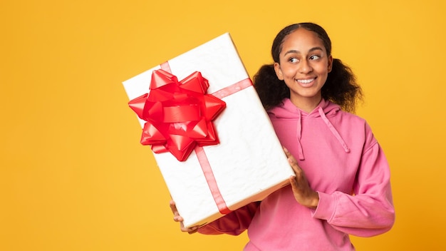 Curious black teenager girl shaking large box checking gift studio