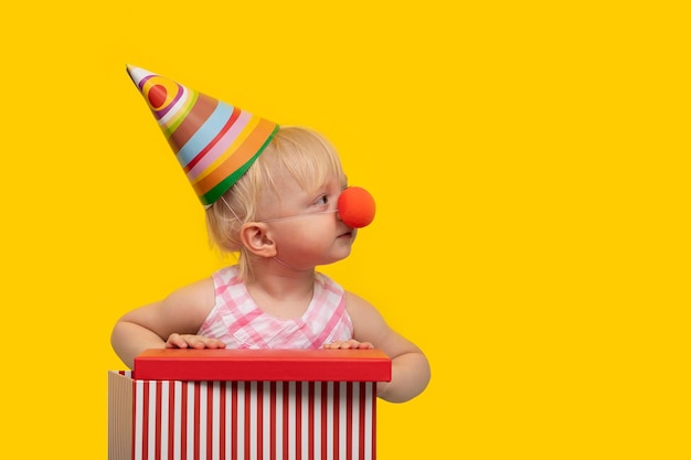 Photo curious child in a festive hat opens gift portrait on yellow background