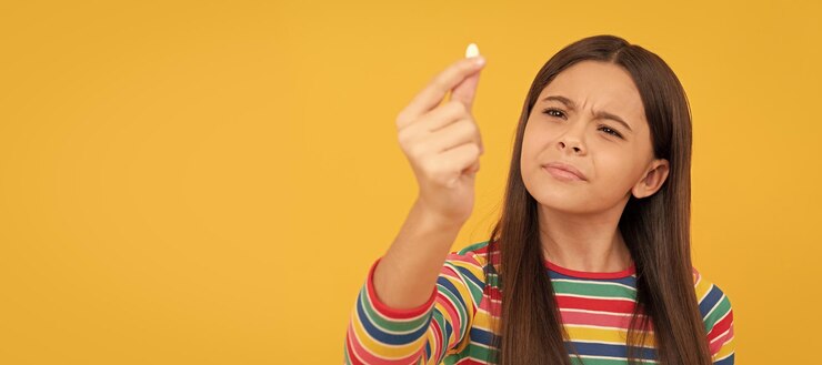 फोटो curious child look at pill capsule shape tablet for kids girl hold multivitamin horizontal poster