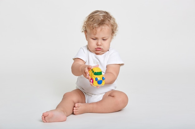 Curious kid playing with toy while sitting on floor