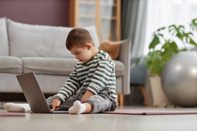 Curious little boy with down syndrome using laptop computer on floor