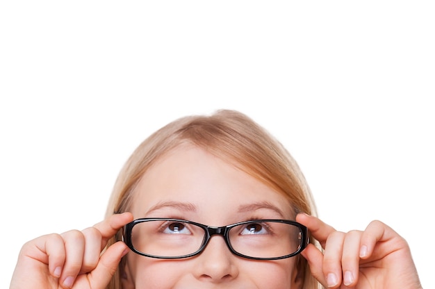 Любопытная маленькая девочка. Обрезанное изображение веселой маленькой девочки, поправляющей очки и смотрящей вверх, изолированной на белом