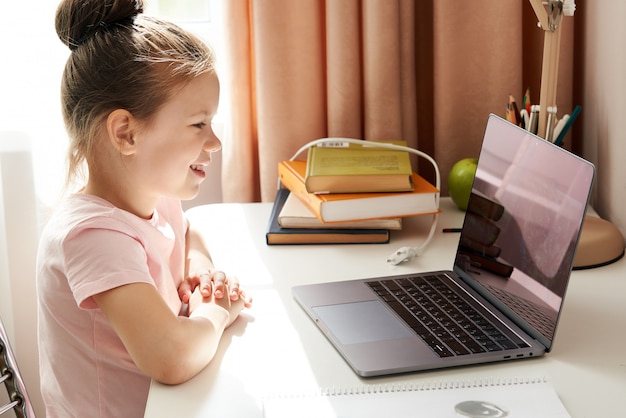 Bambina curiosa che per mezzo del computer portatile allo scrittorio