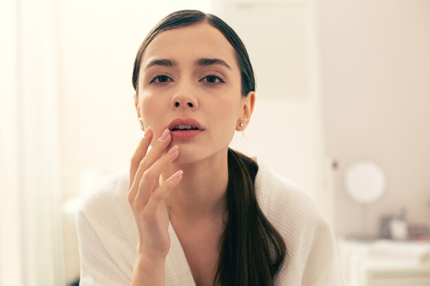 好奇心旺盛な長髪の若い女性が思慮深く唇に触れ、自分の前を見る