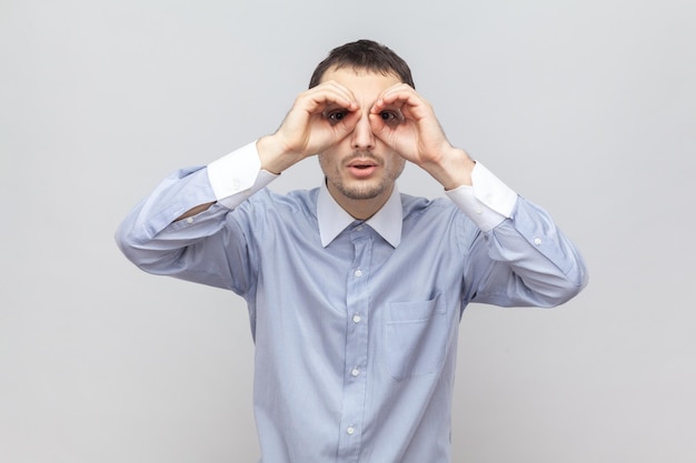 Curious man standing hands near eyes making binocular gesture looking at something interesting