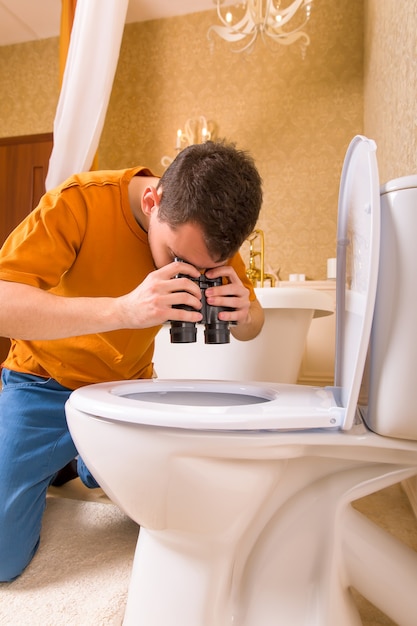Photo curious man with binoculars looking in the toilet. luxury bathroom interior