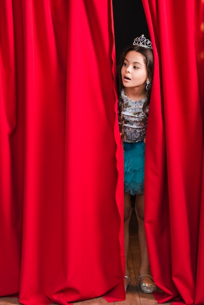 Photo curious pretty girl peeking from red curtain on stage