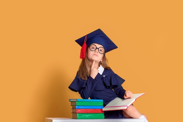 Curious schoolgirl in graduation outfit studying with textbooks