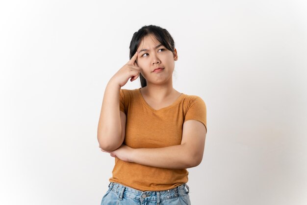 The curious thoughtful young Asian woman looks pensively standing on white background