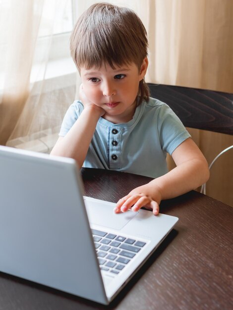 Foto un bambino curioso esplora il portatile e preme i pulsanti della tastiera del computer