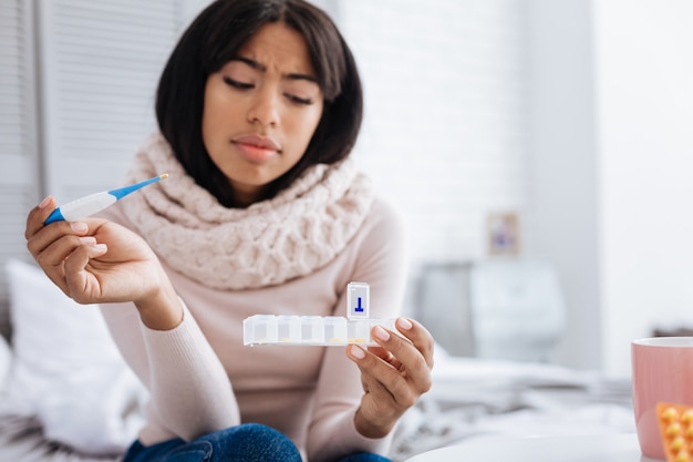 好奇心旺盛な女性。彼女の手でピルボックスを注意深く見ている穏やかな集中若い女性