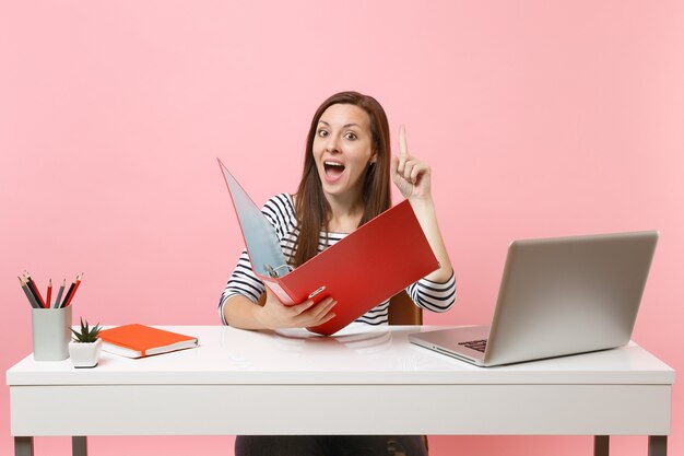 Curious woman pointing finger up holding folder with paper document work on project while sit at office with laptop 