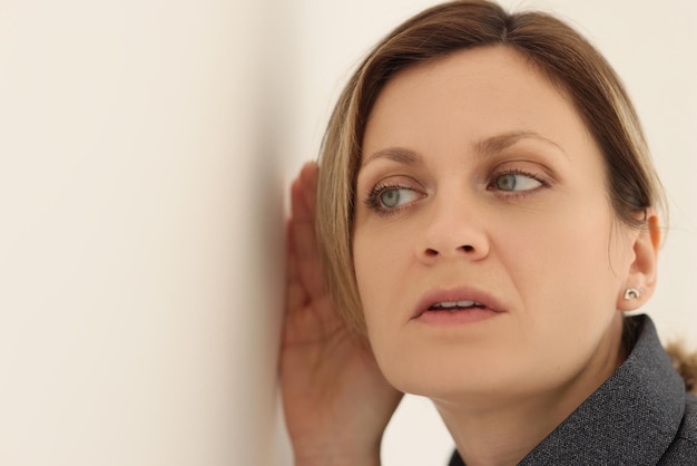 Curious woman tries to eavesdrop on conversation of colleagues behind wall focused female puts