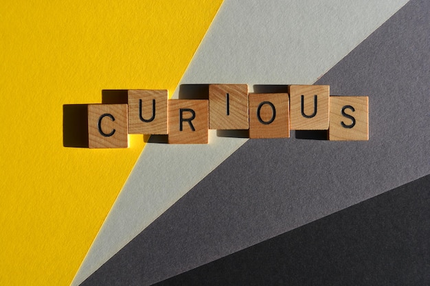 Curious word in wooden alphabet letters isolated on yellow and grey background