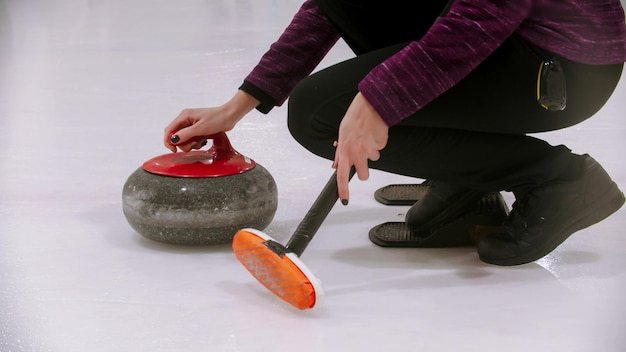 Curling training  woman holding a granite stone with red handle and holding a special brush