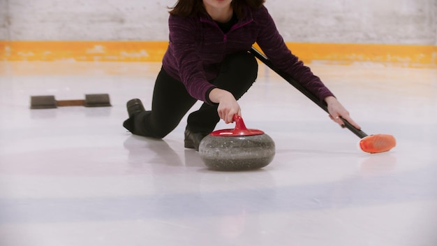 Foto curling formazione donna pattinaggio in possesso di una pietra di granito con manico rosso