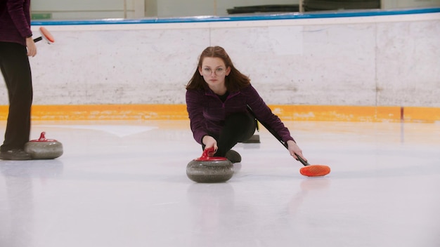 Curling  a young woman in glasses pushes off in the ice field with a granite stone