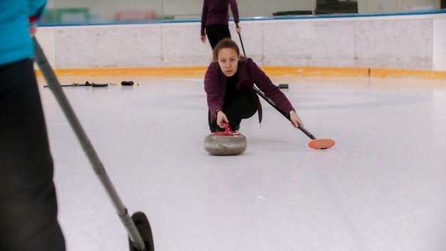 Curling una giovane donna si spinge via nel campo di ghiaccio con una pietra di granito