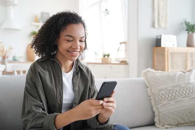 Curly african american girl has fun with phone at home and smiling Communication concept