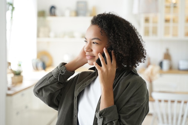 Curly afro girl has phone call at kitchen at home and listening to friend Remote conversation