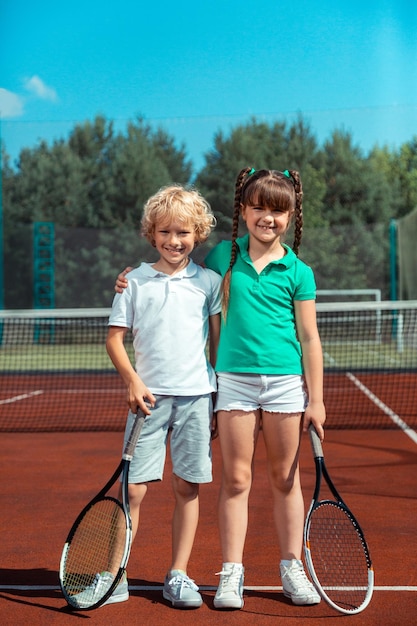 Кудрявый блондин, стоящий рядом с девушкой, стоящей на теннисном корте