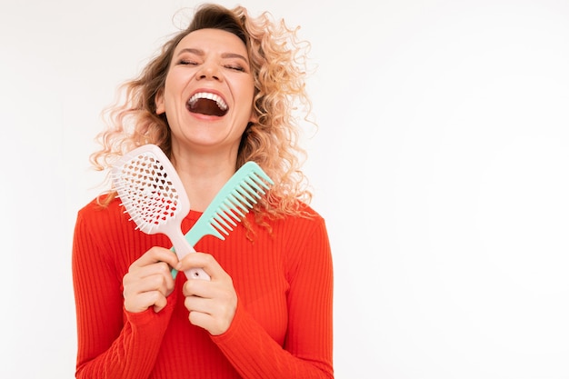 Curly blonde girl holds hair combs in her hands on a white background with copyspace