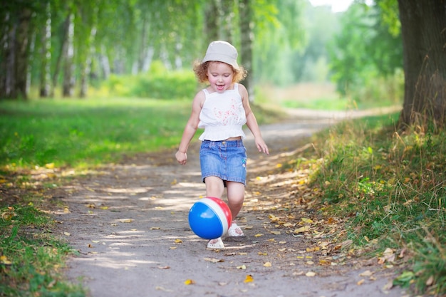 夏の公園でゴムボールで遊ぶ巻き毛のブロンドの女の子