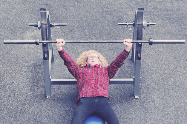 Photo curly blonde guy in a red shirt trying to raise the barbell with effort toned