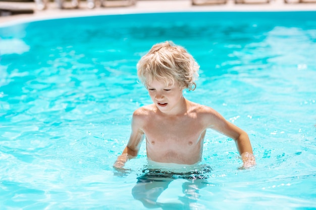 太陽を楽しんで、プールで泳ぐ巻き毛の少年