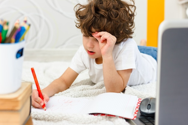 Curly boy is engaged at computer. schoolboy grabs his head in surprise. Concept of difficulties of home schooling, distance studying.