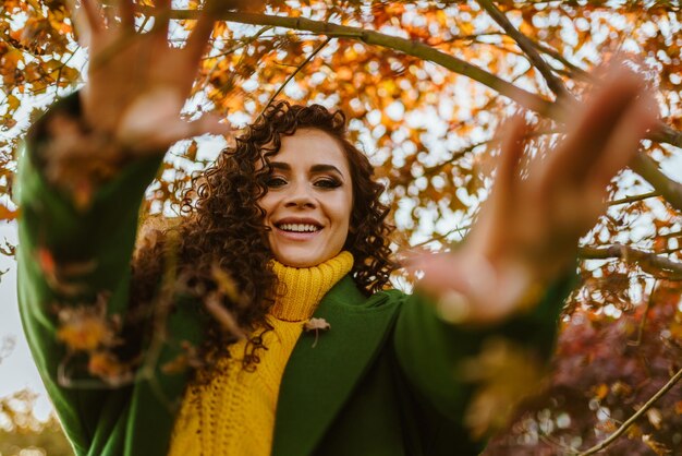 The curly brunette smiles happily and pulls her hands to the camera on her clad green coat on a brig