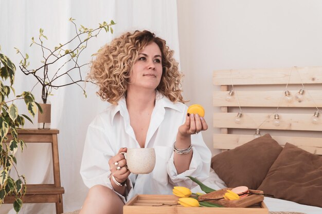 Curly European woman having breakfast in bed in hotel