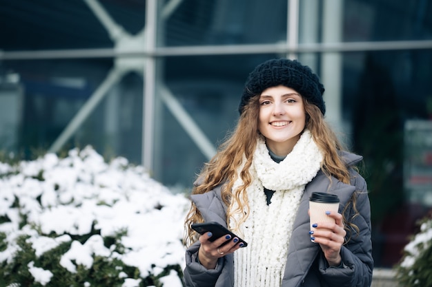 Curly female using smartphone standing outside.