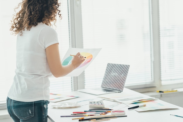 The curly girl with a brush drawing a picture at the table