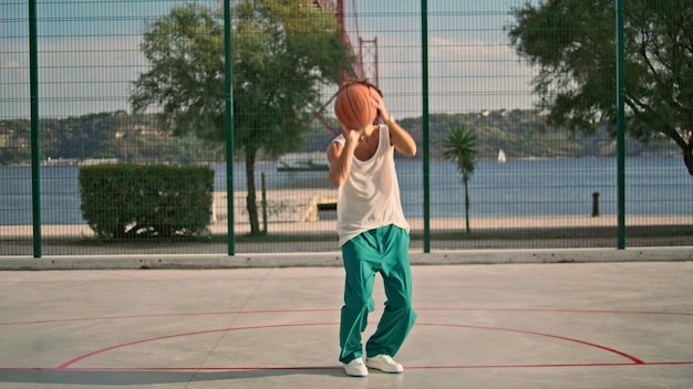 Кудрявый парень играет в баскетбол на спортивной площадке, умелый подросток бросает мяч