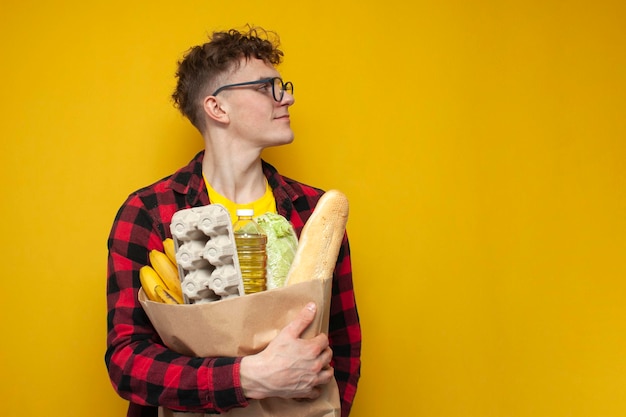 Curly guy with package of groceries stands on yellow background and looks away at copy space