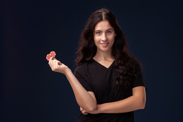 Curly hair brunette is posing with red gambling chips in her hands. Poker concept on a black background. Casino.