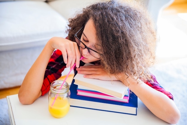 Foto la ragazza teenager dei capelli ricci beve il succo e riposa sui libri