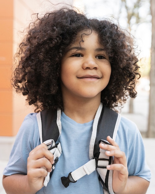 Curly haired boy back to school, preschool, grabbing his backpack happy smiling