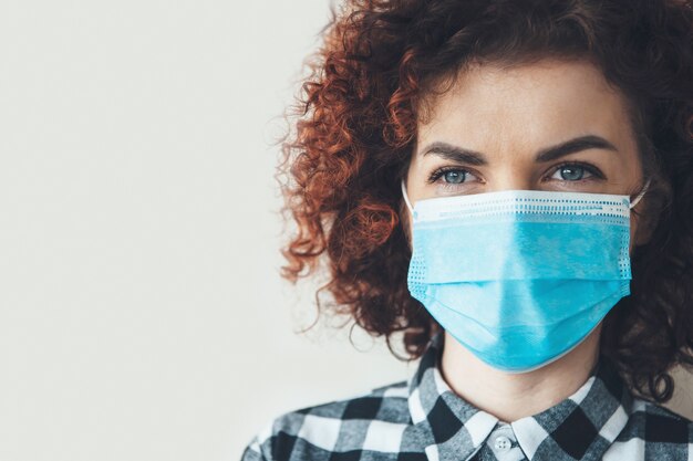 Curly haired brunette vrouw poseert dicht bij de camera op een grijze studiomuur met vrije ruimte in een masker