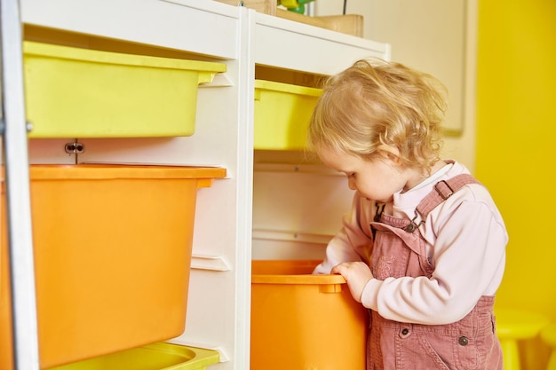 Curly-haired girl is digging in a box with toys.