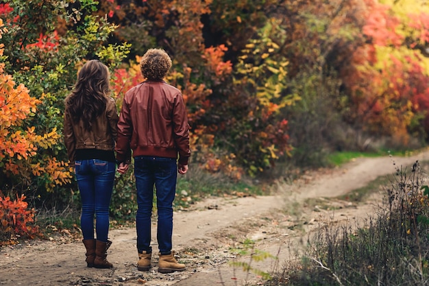 Curly-haired guy and fair-haired girl in autumn standing unfolded with their backs on road