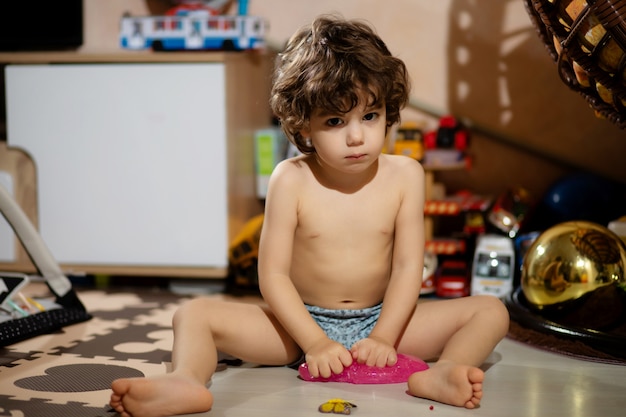 Curly-haired little boy in shorts plays with slime in his room